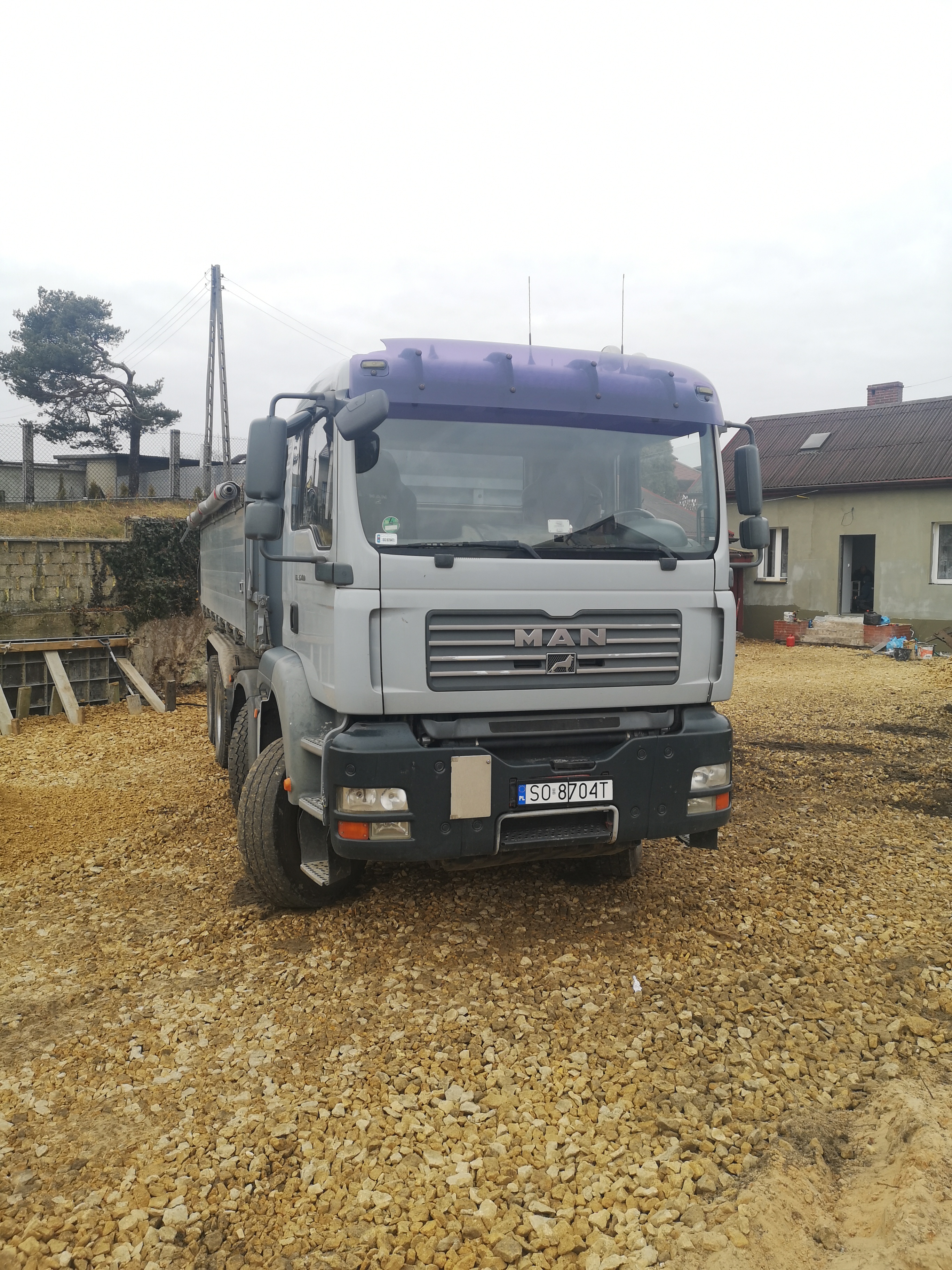 Szary samochód ciężarowy marki MAN na placu budowy z wysypanym kruszywem, widoczny numer rejestracyjny SO 8704T