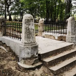 Kamienne schody z balustradą na cmentarzu, widoczne ślady napraw i renowacji, otoczone drzewami.