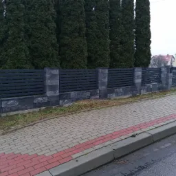 Nowoczesne ogrodzenie panelowe z poziomymi przęsłami w kolorze antracytowym, wsparte na słupkach z szarej kostki, na tle rzędu wysokich, zielonych tuj.