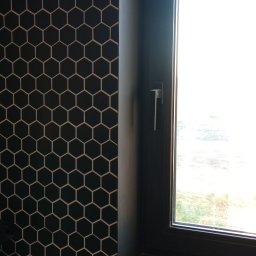 Remont4you - Czarne heksagonalne płytki z jasną fugą na ścianie i parapecie okiennym w łazience. Nowoczesne wykończenie wnętrza, okno z czarną ramą.