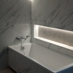 Remont4you - Wykończona łazienka z wanną obudowaną płytkami imitującymi marmur, podświetleniem LED na suficie i wnęką w ścianie. Widoczne narzędzia glazurnicze.