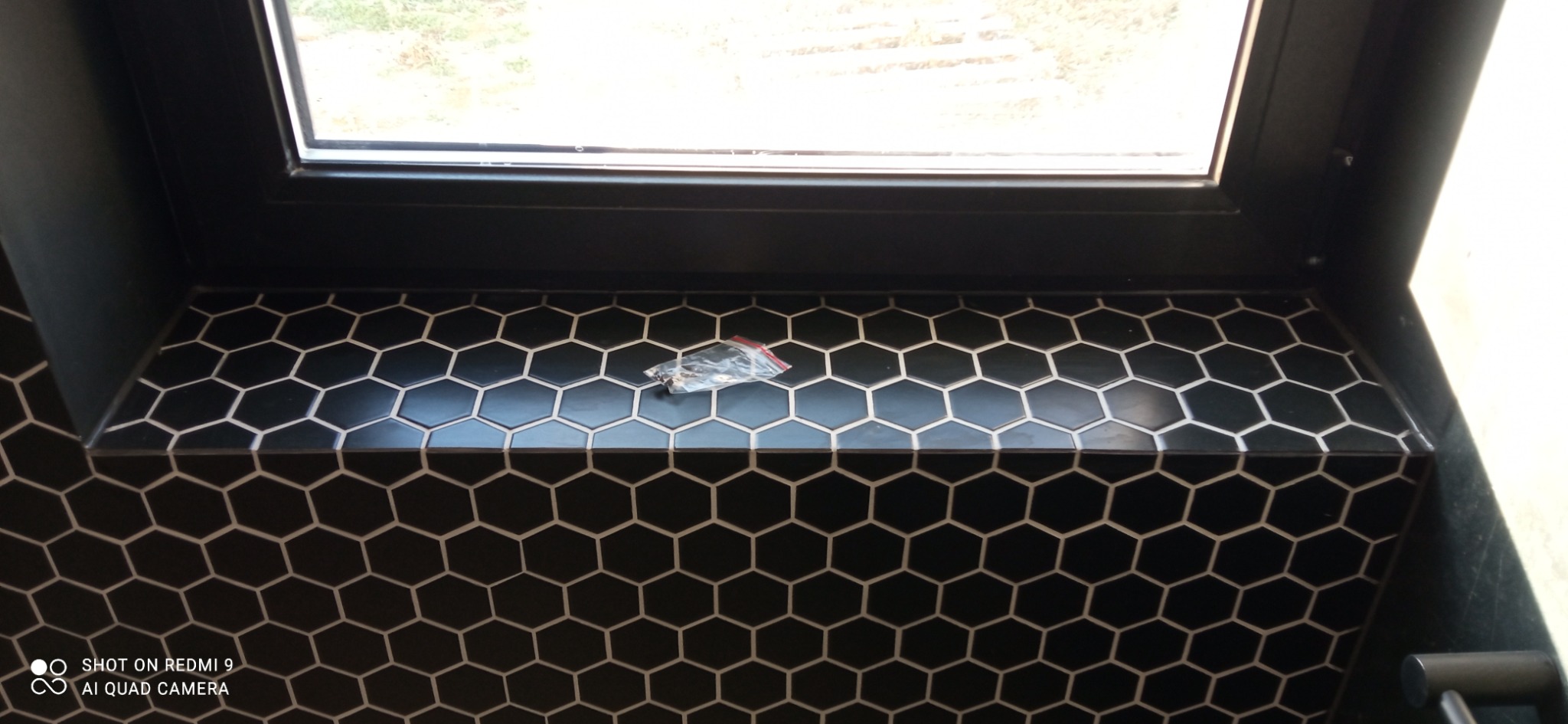 Czarna, heksagonalna mozaika na parapecie pod oknem, z pakietem akcesoriów. Nowoczesne wykończenie wnętrza, detale glazurnicze, precyzyjne ułożenie płytek.