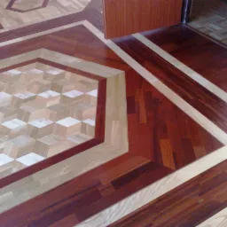 Wzorzysta podłoga z parkietu ułożonego w geometryczne wzory, z efektem 3D w centralnej części, widziana z perspektywy lekko skośnej, z fragmentem drzwi w tle.