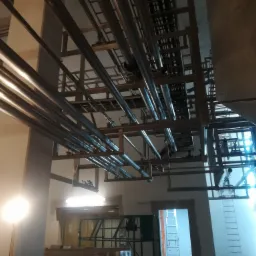 Konstrukcja stalowa z rurami w hali produkcyjnej w Seroczynie. Widok z dołu na metalową konstrukcję pod sufitem, z licznymi rurami i elementami mocującymi.