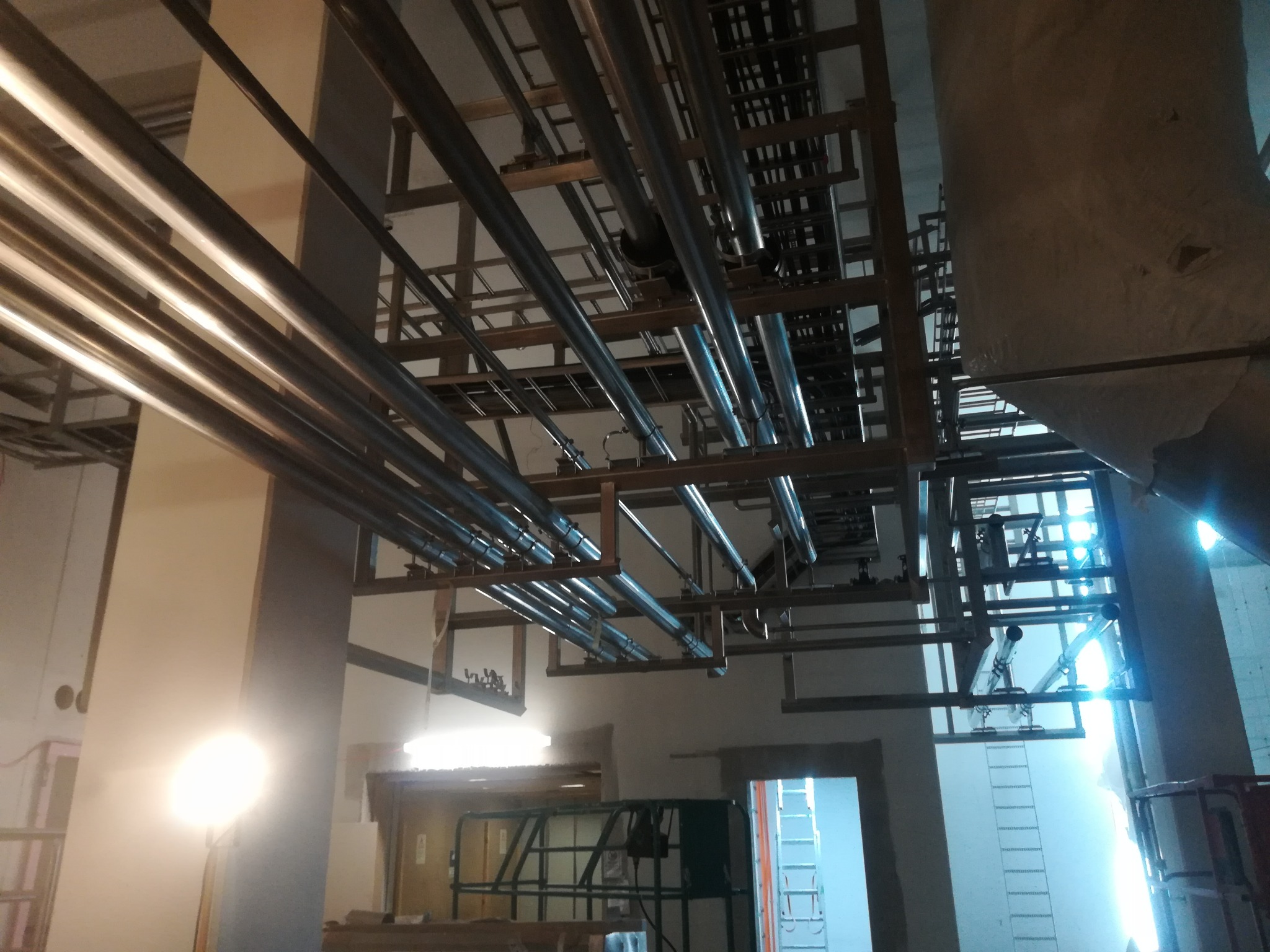 Konstrukcja stalowa z rurami w hali produkcyjnej w Seroczynie. Widok z dołu na metalową konstrukcję pod sufitem, z licznymi rurami i elementami mocującymi.