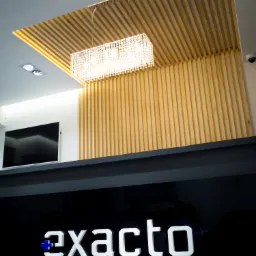 Nowoczesny wystrój poczekalni gabinetu stomatologicznego Exacto w Poznaniu, z dekoracyjnym oświetleniem sufitowym, drewnianymi panelami i podświetlanym logo firmy.