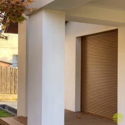 MARKIZA.PL SPÓŁKA Z OGRANICZONĄ ODPOWIEDZIALNOŚCIĄ - Zewnętrzna roleta antywłamaniowa w kolorze brązowym, zamontowana w nowoczesnym domu z białymi kolumnami, widok z boku w słoneczny dzień.