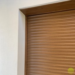 MARKIZA.PL SPÓŁKA Z OGRANICZONĄ ODPOWIEDZIALNOŚCIĄ - Fragment zamkniętej, poziomej rolety o strukturze drewna, zamontowanej w ościeżnicy o podobnym wykończeniu, widok z bliska na narożnik.