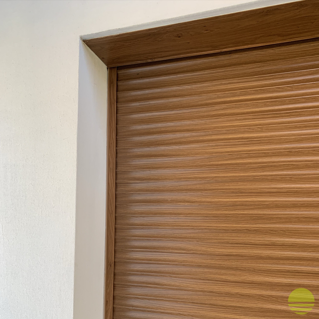 Fragment zamkniętej, poziomej rolety o strukturze drewna, zamontowanej w ościeżnicy o podobnym wykończeniu, widok z bliska na narożnik.