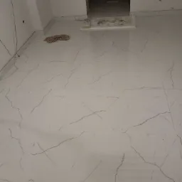 Nowo położona, błyszcząca, biała podłoga z płytek imitujących marmur z wyraźnym wzorem żyłkowania, widoczne kable na ścianie, szmata i próg w tle.