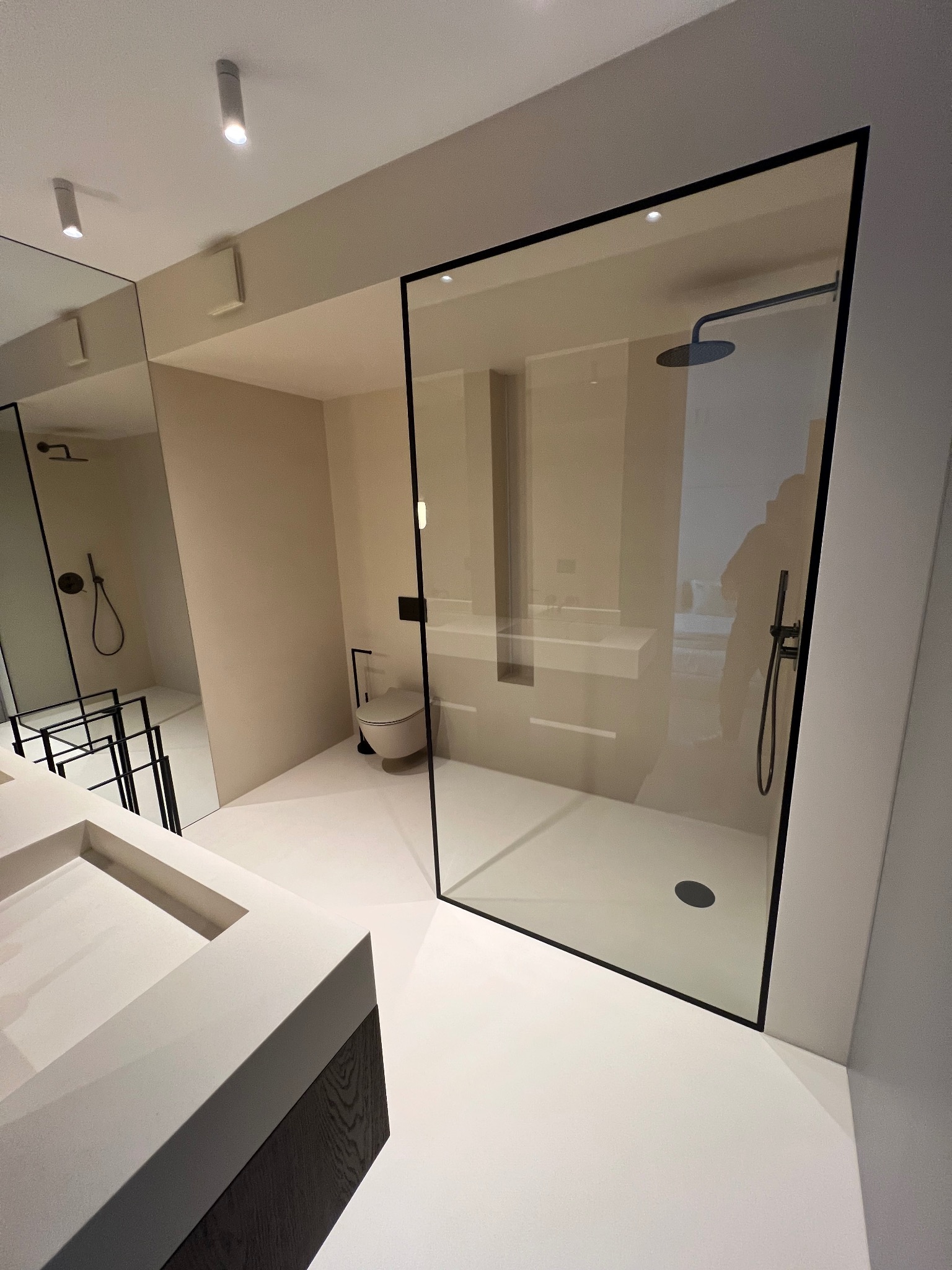 Minimalistyczna łazienka z kabiną prysznicową typu walk-in z czarną ramą, umywalką wpuszczaną w blat i toaletą w neutralnej kolorystyce.