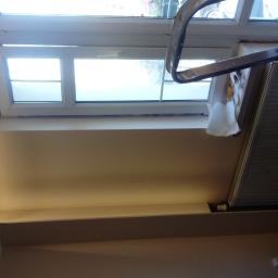 KSAPAT - Świeżo pomalowana ściana przy oknie z grzejnikiem, widoczna drabina malarska i zabezpieczenia.