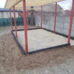 Przygotowany teren pod garaż z drewnianą konstrukcją, obrzeżami z kostki i podsypką piaskową, widok z boku.