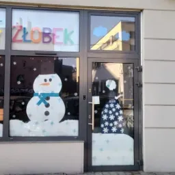 Fasada budynku z świątecznymi dekoracjami okiennymi: choinka, bałwan i niedźwiedź polarny w czapce.