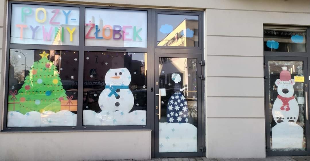 Fasada budynku z świątecznymi dekoracjami okiennymi: choinka, bałwan i niedźwiedź polarny w czapce.