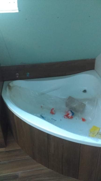 Narożna wanna obudowana panelami imitującymi drewno, w trakcie prac wykończeniowych, widoczne drobne śmieci i folia ochronna wewnątrz wanny.