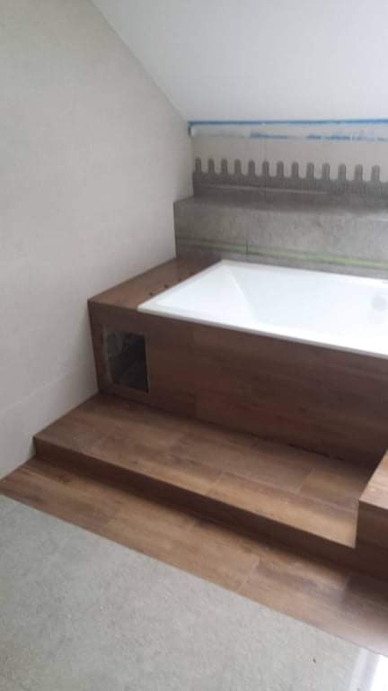 Wykończenie wnęki w łazience z zabudowaną wanną, wyłożoną brązowymi płytkami imitującymi drewno, widoczny otwór rewizyjny, na ścianie widoczny fragment przygotowania pod glazurę.