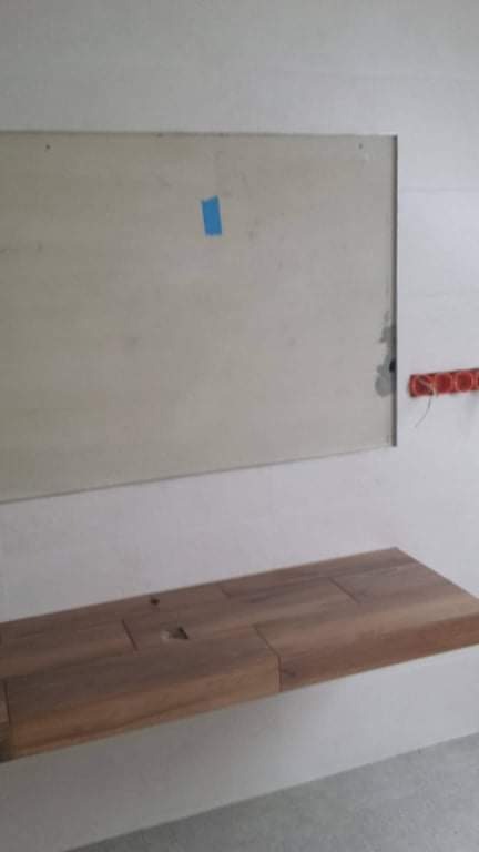 Płyta gipsowa na ścianie z niebieską taśmą maskującą, drewniany blat pod umywalkę, instalacja elektryczna w puszce w tle.