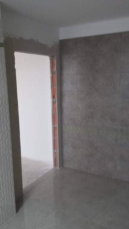 Ściana w łazience wyłożona szarymi płytkami imitującymi kamień, widoczny fragment futryny drzwi.