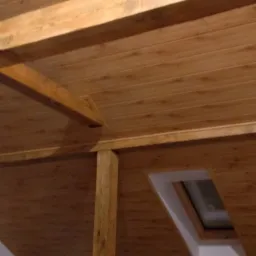 Wykończone drewniane poddasze z widocznym oknem dachowym i belkami konstrukcyjnymi, widok pod kątem.