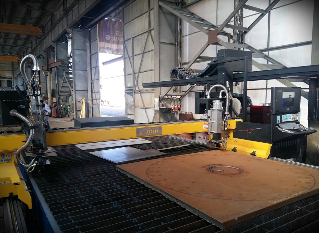 Automatyczna maszyna do cięcia plazmowego marki Ajan w hali produkcyjnej, wycinająca okrągły element ze stalowej blachy. Widoczne ślady cięcia plazmą.