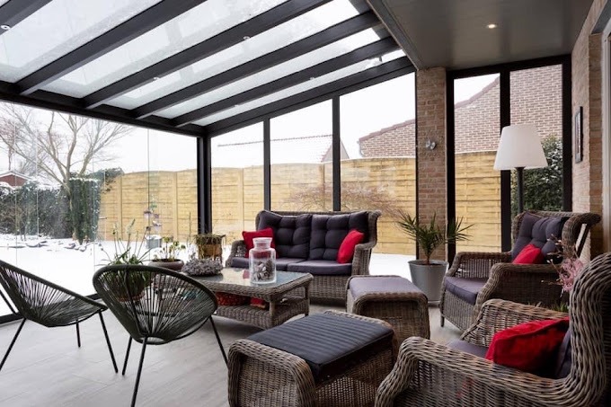 Zimowy ogród w Poznaniu z zadaszeniem z czarnymi belkami, wyposażony w wiklinowe meble wypoczynkowe z czerwonymi poduszkami, nowoczesne krzesła z plecionki i szklany stolik kawowy.