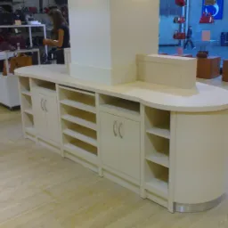 Jasny, zabudowany mebel sklepowy z półkami i szafkami, widoczny w tle sklep z torebkami i osoba przy półkach.