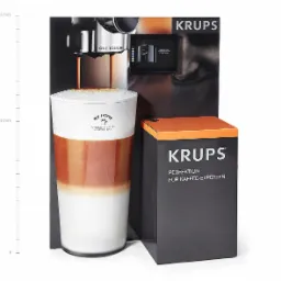 Prezentacja ekspresu Krups One Touch z wysoką szklanką Latte Macchiato, obok pudełko z napisem Krups Perfektion für Kaffee-Experten.