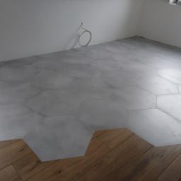 FHU Dawid Bigos - Pokój w trakcie wykańczania z szarymi, heksagonalnymi płytkami częściowo ułożonymi na podłodze, obok widoczna drewniana podłoga.