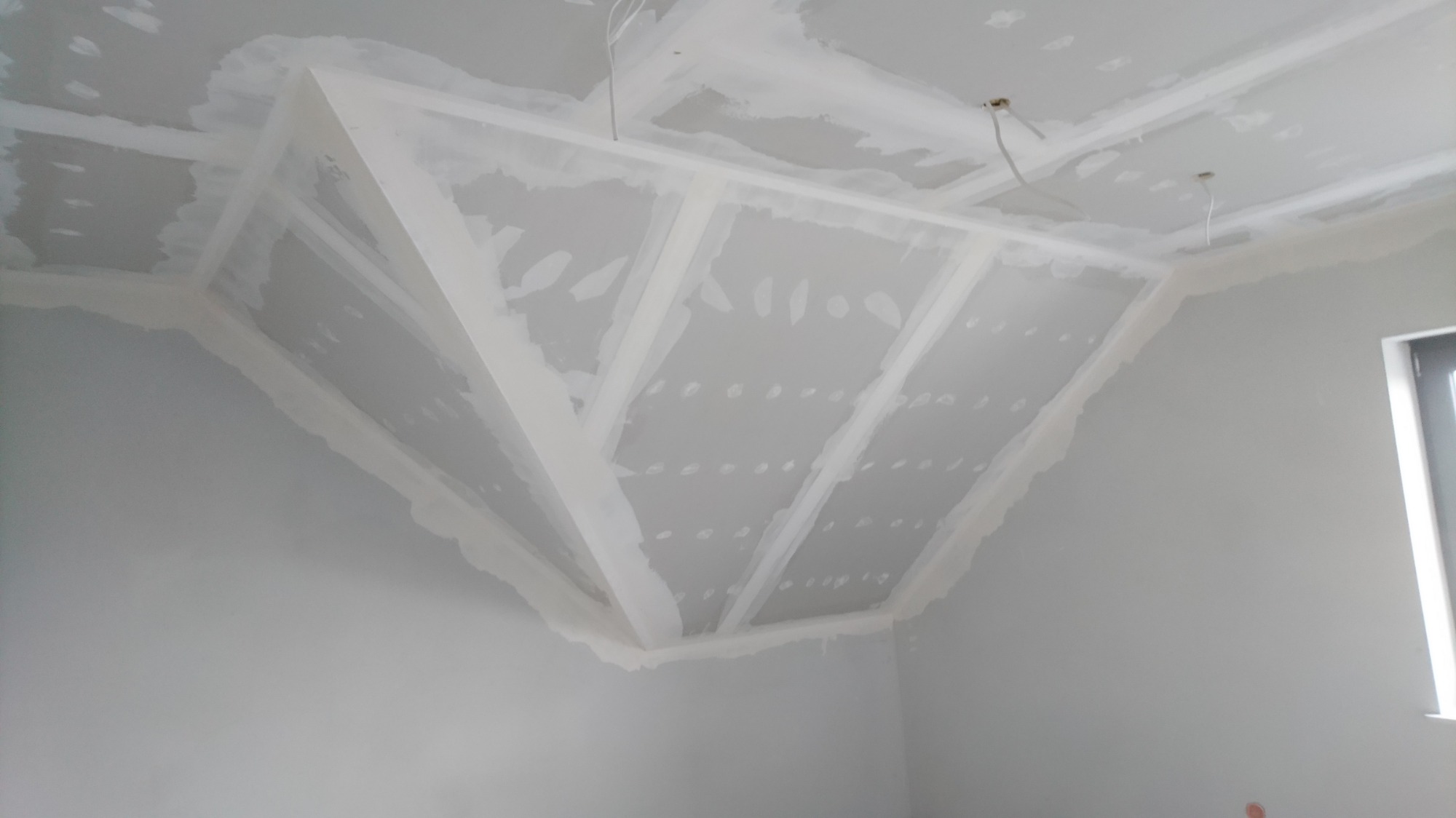 Sufit podwieszany z płyt kartonowo-gipsowych w trakcie montażu, widoczne łączenia wzmocnione taśmą, przygotowany do szpachlowania, zarys okna w tle.