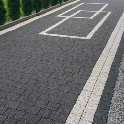 Ułożona kostka brukowa w Przemyślu z dekoracyjnym wzorem białych kwadratów i jasnymi pasami po bokach, obok zielony żywopłot.