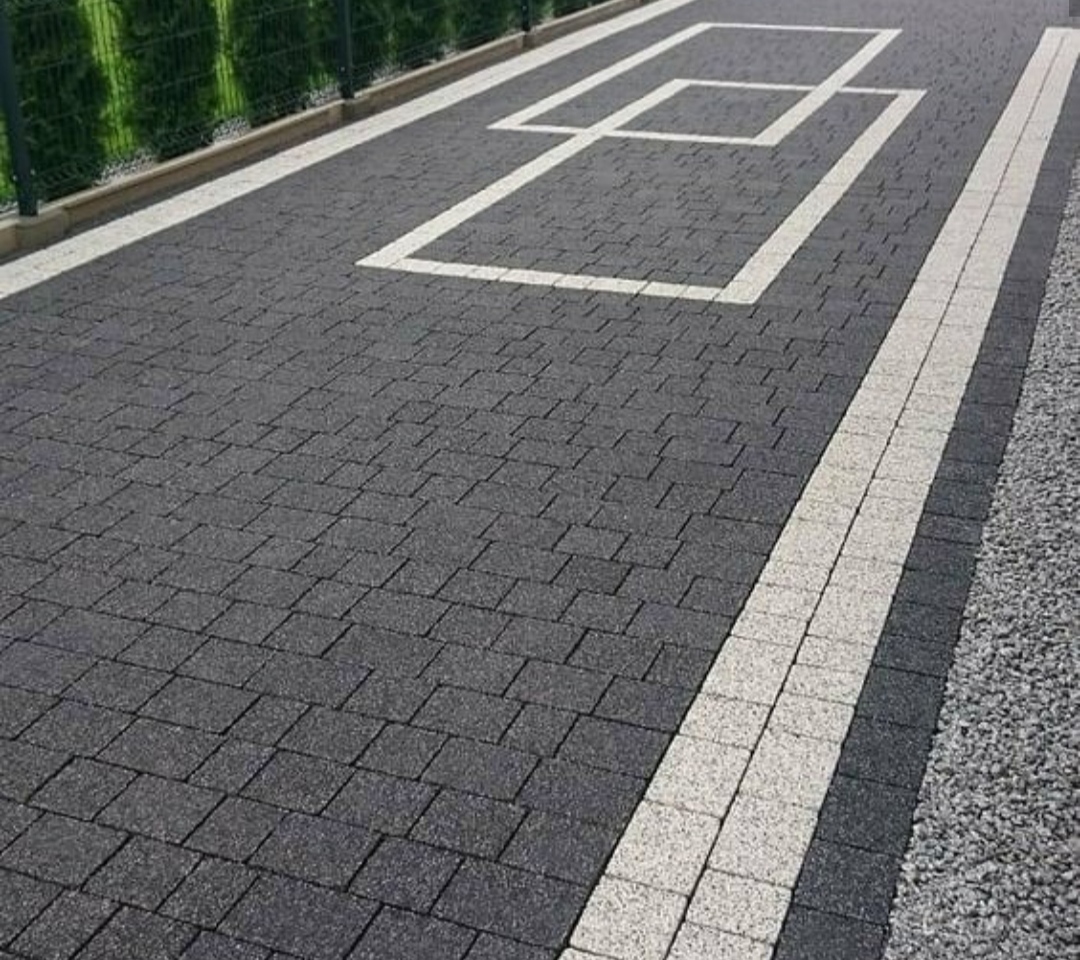 Ułożona kostka brukowa w Przemyślu z dekoracyjnym wzorem białych kwadratów i jasnymi pasami po bokach, obok zielony żywopłot.