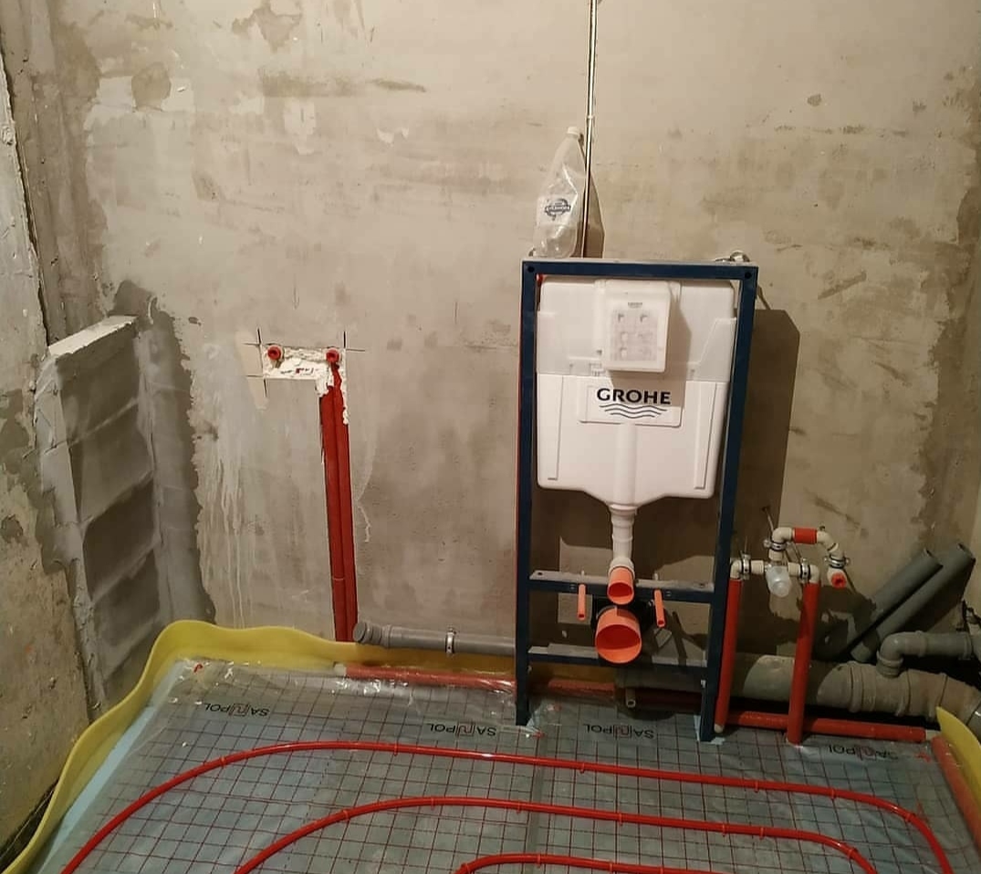 Montaż podtynkowego stelaża WC marki Grohe z instalacją ogrzewania podłogowego w surowej łazience z betonowymi ścianami.