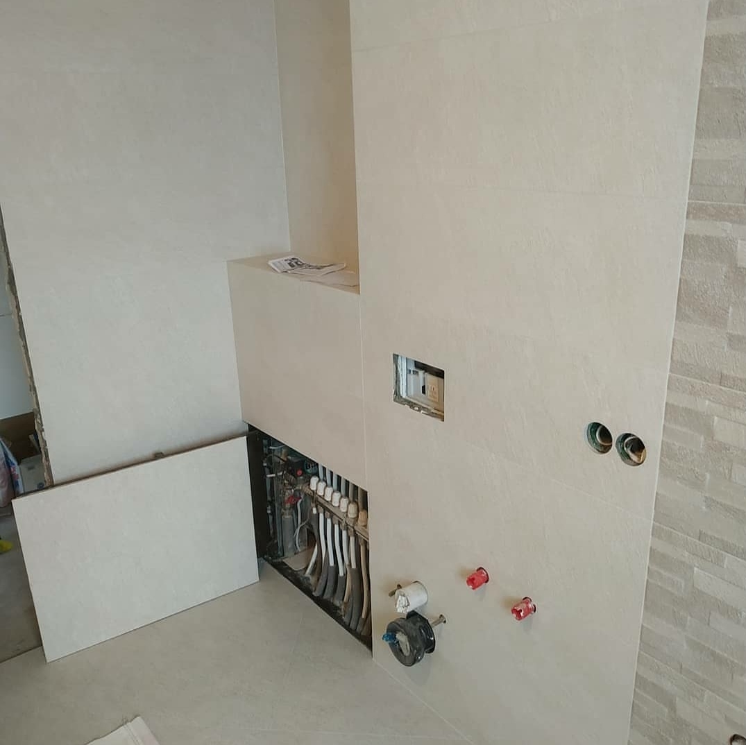 Wnętrze łazienki w trakcie wykańczania, z widoczną instalacją ogrzewania podłogowego za obudową z płytek i przygotowanymi punktami wodno-kanalizacyjnymi na ścianie.