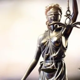 Statuetka Temidy z zasłoniętymi oczami, trzymająca wagę sprawiedliwości, w ciepłym oświetleniu z rozmytym tłem.