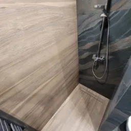 Nowoczesna kabina prysznicowa z odpływem liniowym, wykończona płytkami imitującymi drewno i kamień, z chromowaną armaturą.