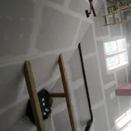 Poddasze w trakcie wykańczania: widoczne drewniane rusztowanie, częściowo zamontowane płyty gipsowo-kartonowe na skosach i ścianach, oraz okna dachowe. Szpachlowane łączenia płyt i widoczne...