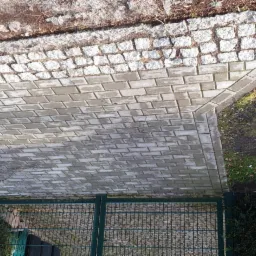 Widok z góry na ścieżkę z szarej kostki brukowej prowadzącą do zielonej bramy, obrzeże z kostki granitowej, trawa po bokach.