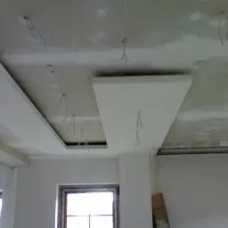 Niedokończony sufit podwieszany z wystającymi przewodami elektrycznymi w nowym domu, widoczne okno i rusztowanie