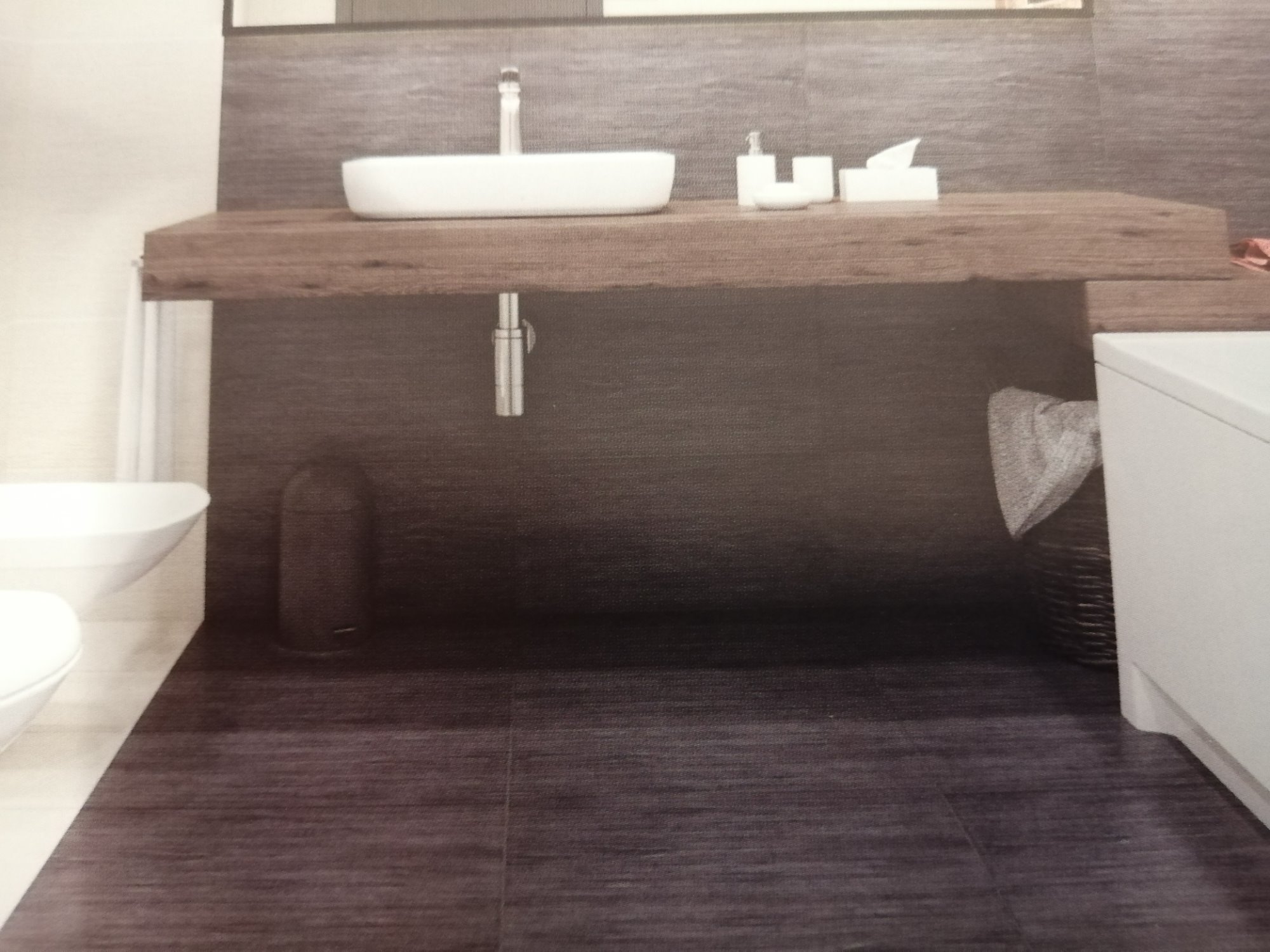 Nowoczesna łazienka z ciemnymi płytkami imitującymi drewno na podłodze i ścianie, biała umywalka nablatowa na drewnianym blacie, widoczny fragment toalety i kosza na pranie.