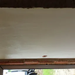 Świeżo położona, jasna gładź na suficie z widocznymi śladami szpachlowania, zarys okna w dolnej części kadru i fragmentem muru z cegieł.