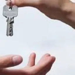 Przekazywanie klucza przez dwie osoby; jedna ręka podaje klucz, druga go odbiera, jasne tło.