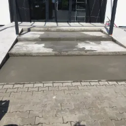Wylewka betonowa na schodach wejściowych do budynku, widok z góry na świeży beton i kostkę brukową przed schodami.