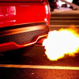 Czerwony samochód z płomieniami wydobywającymi się z rury wydechowej, widziany na ulicy w Pułtusku.