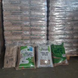 Stosy worków pelletu drzewnego różnych producentów, w tym Radziszewski, Pelet Mazur i Liściasto-Iglasty, zapakowane w folię i ułożone na paletach, widoczne etykiety z certyfikatami EN A1 plus.