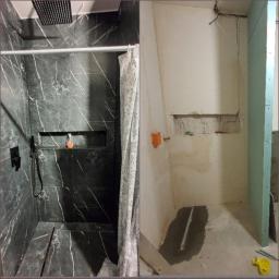 An-Bud - Łazienka w trakcie remontu: po lewej wykończona strefa prysznicowa z czarnymi płytkami imitującymi marmur i deszczownicą, po prawej surowe ściany z instalacją elektryczną i fragmentem płyty...