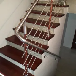 Nowoczesne schody drewniane z metalową balustradą, widok z dołu, z ciemnym kotem siedzącym na dolnych stopniach.