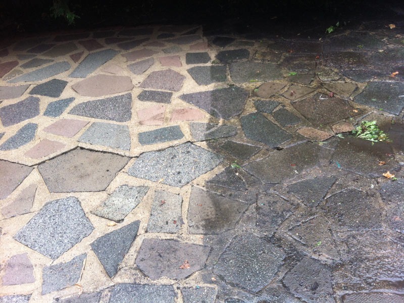 Częściowo wyczyszczona kostka brukowa z kamiennymi płytami o nieregularnych kształtach; widoczna różnica w kolorze i wyglądzie między czystą i brudną powierzchnią.
