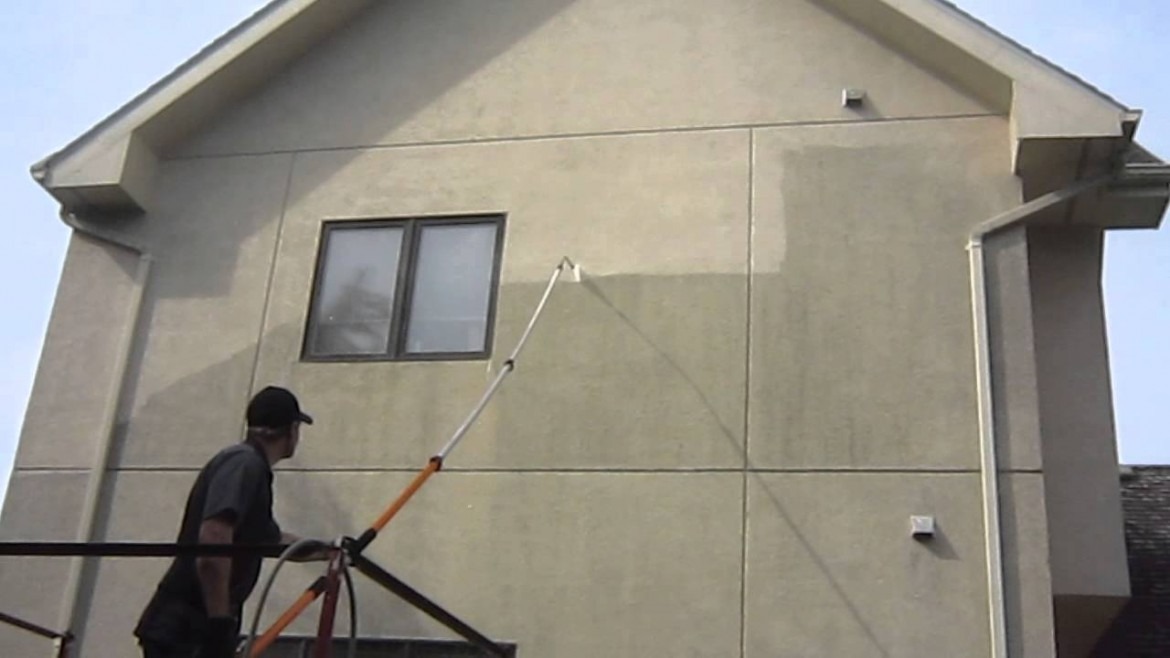 Pracownik na rusztowaniu czyści elewację budynku za pomocą lancy teleskopowej; widoczna wyraźna różnica w kolorze pomiędzy umytą a brudną powierzchnią.
