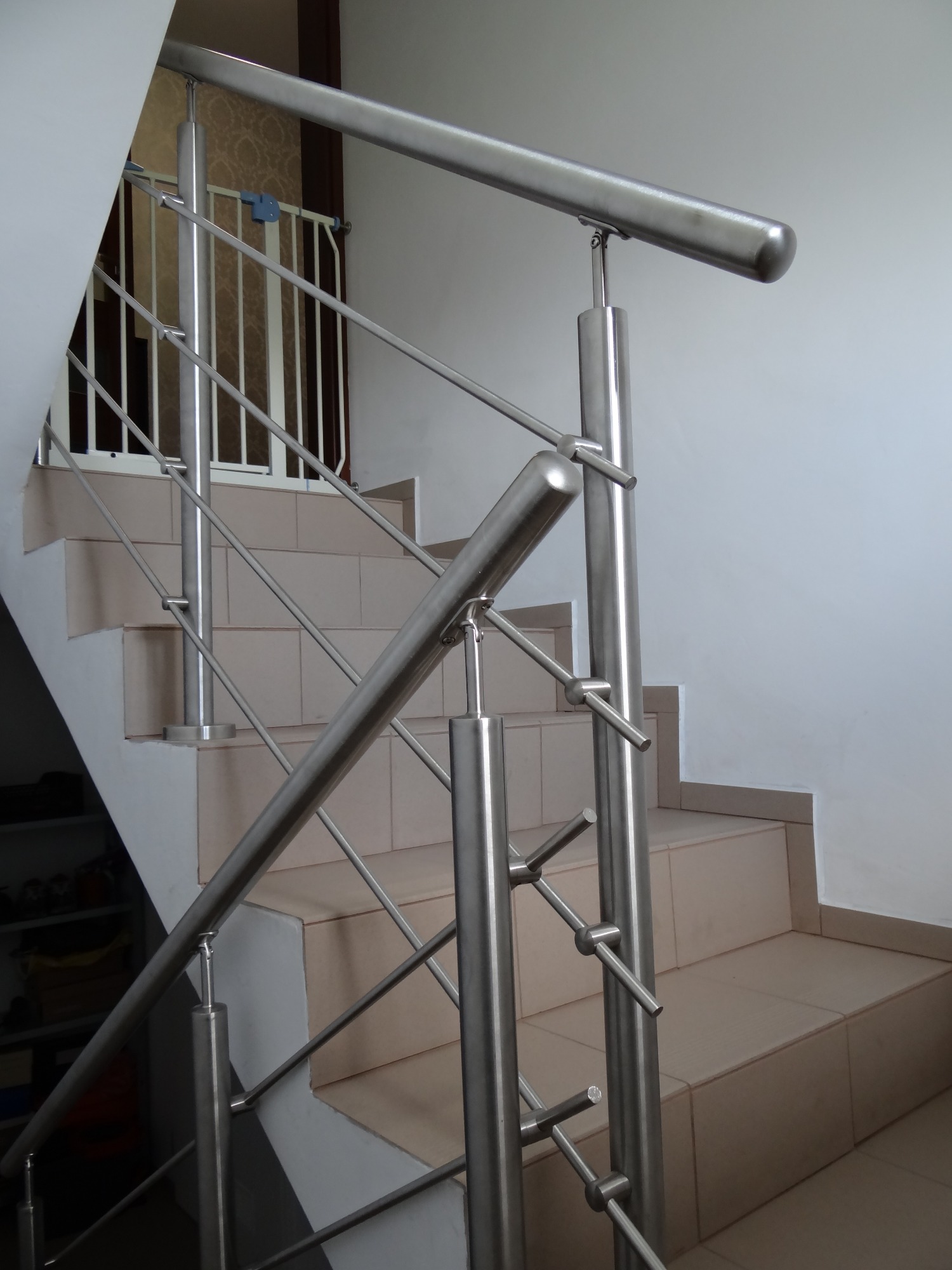 Schody wyłożone beżowymi płytkami z zamontowaną, nowoczesną, metalową balustradą z okrągłą poręczą i zabezpieczeniem schodów dla dzieci w tle.